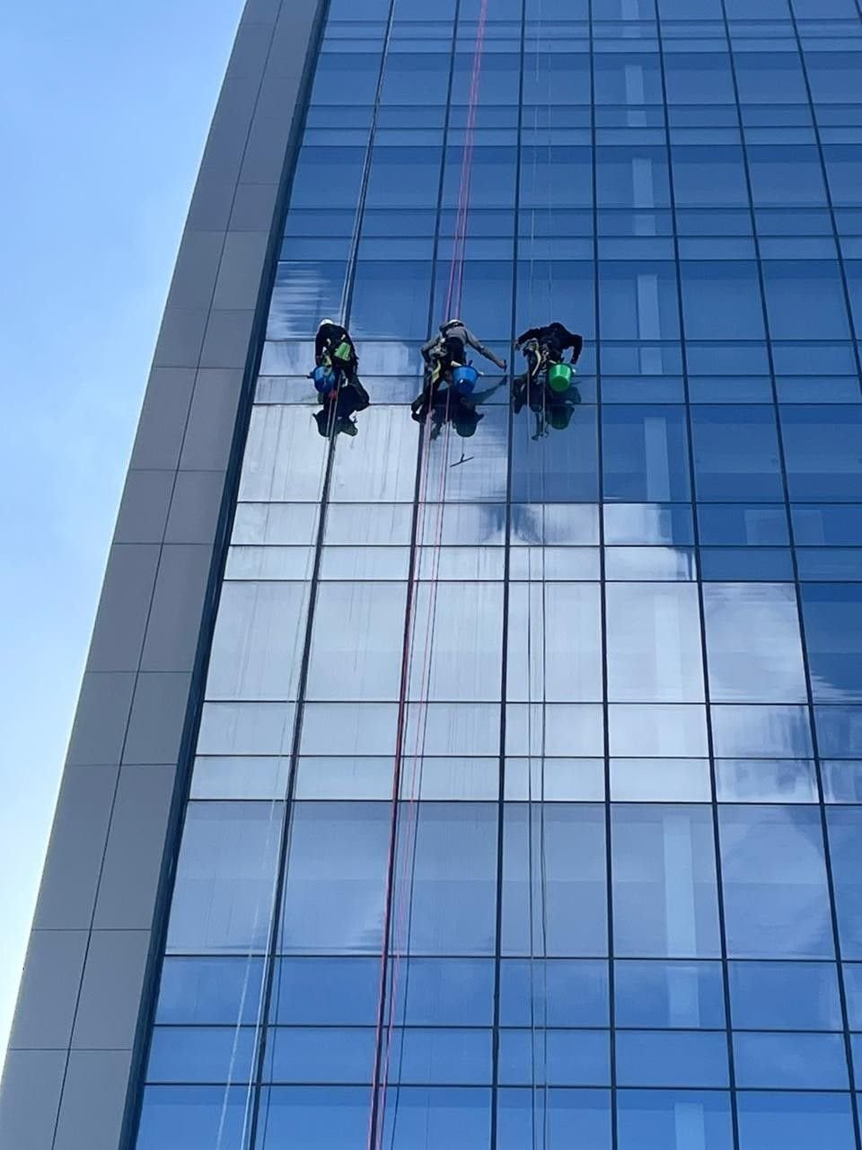 Three technicians abseiling down a glass tower
