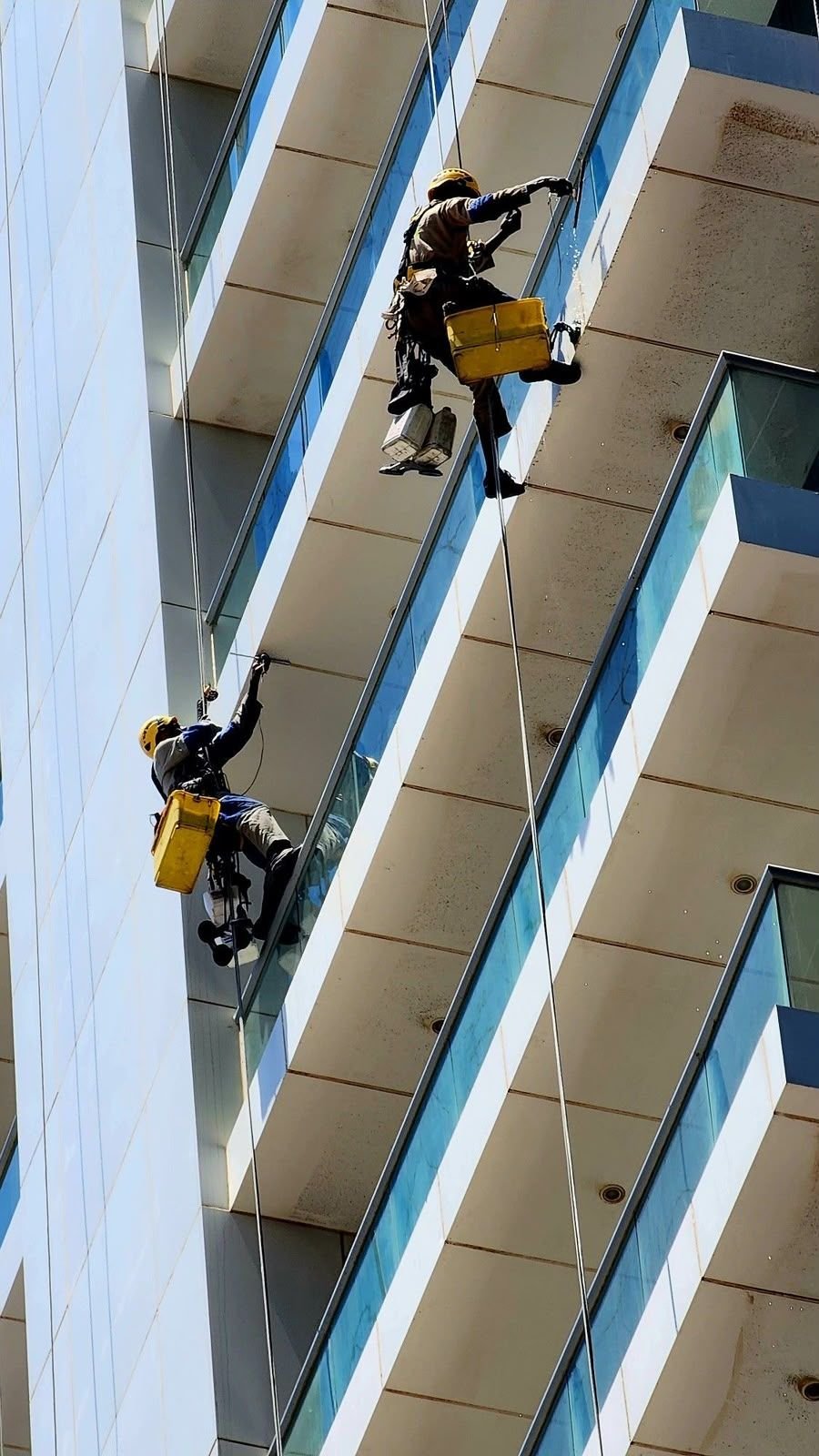 Rope access team cleaning cladding panels in bright sun