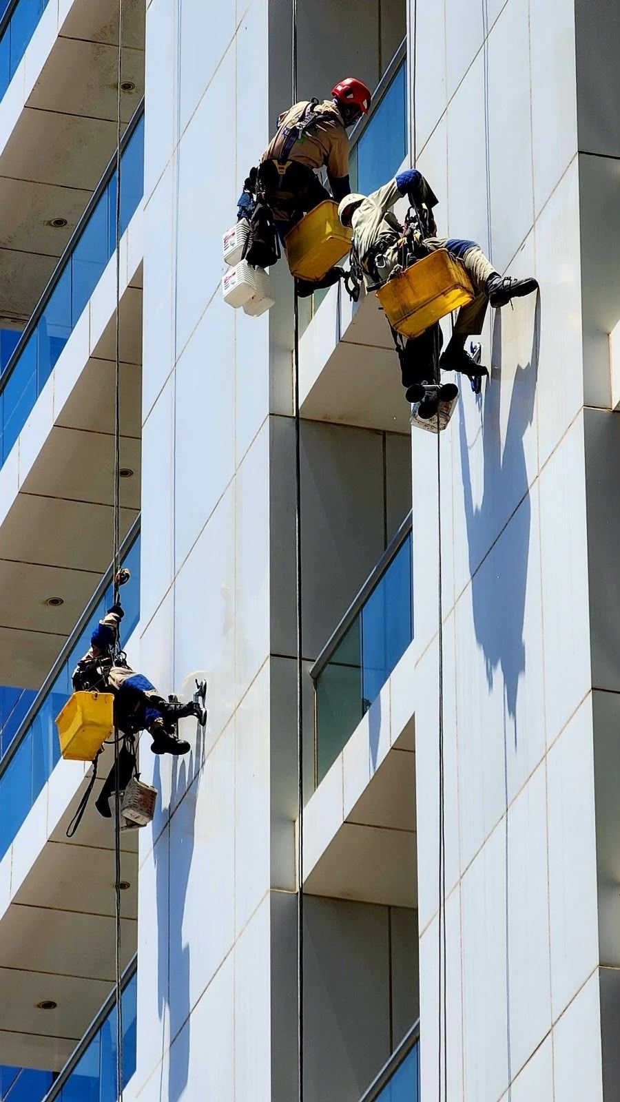Two rope access technicians cleaning a high-rise balcony façade